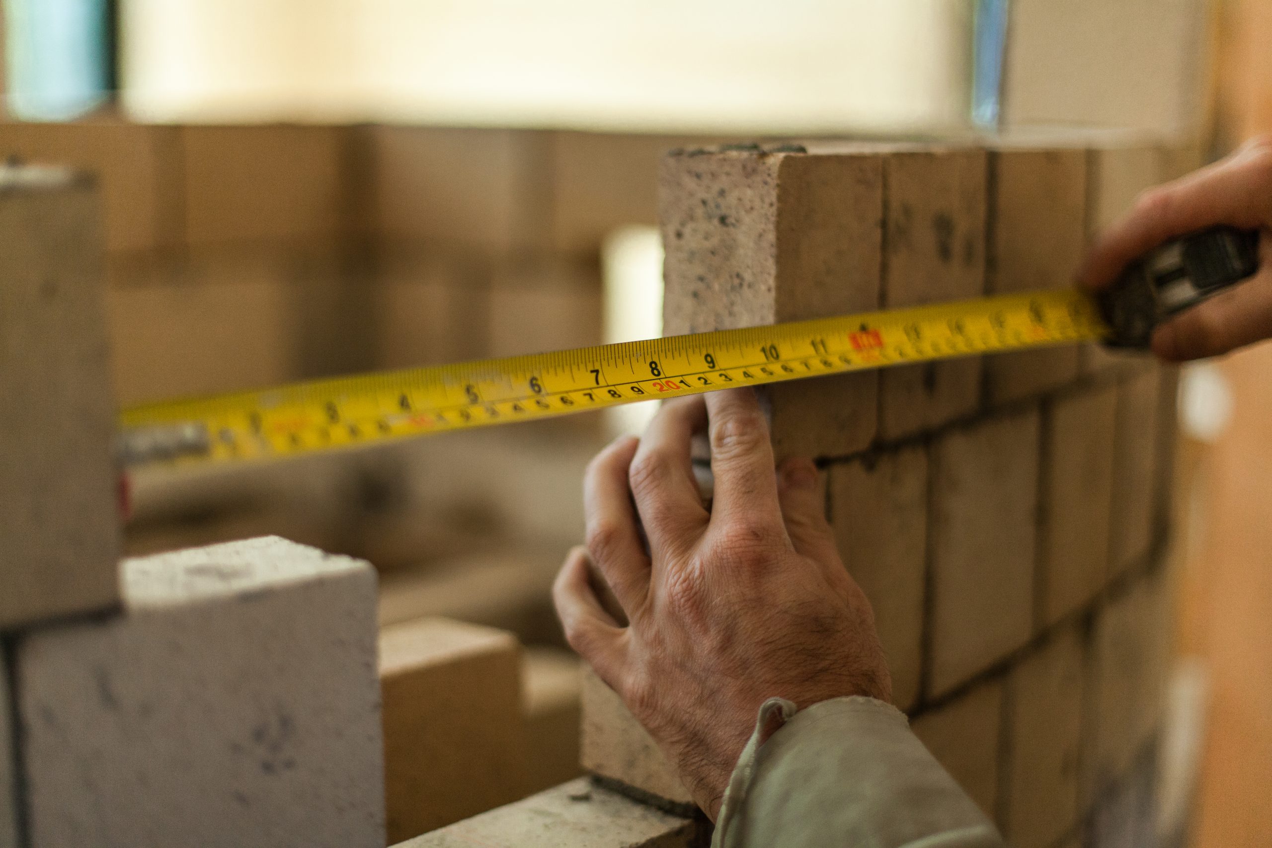 Brickmason,Holding,A,Measuring,Tape,To,Calculate,The,Distance,Between