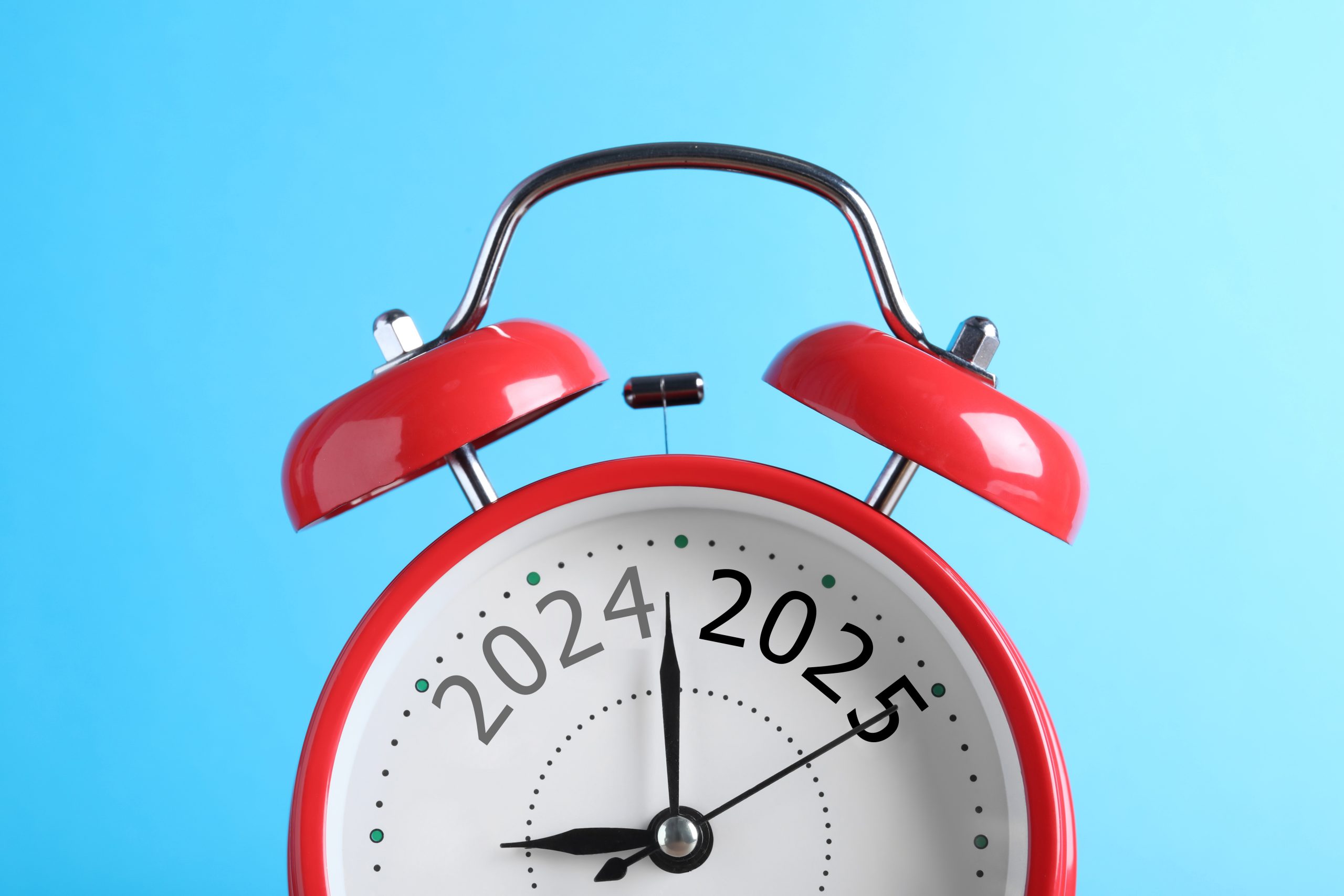 Red alarm clock with numbers 2024 and 2025 on light blue background, closeup. Beginning of new year
