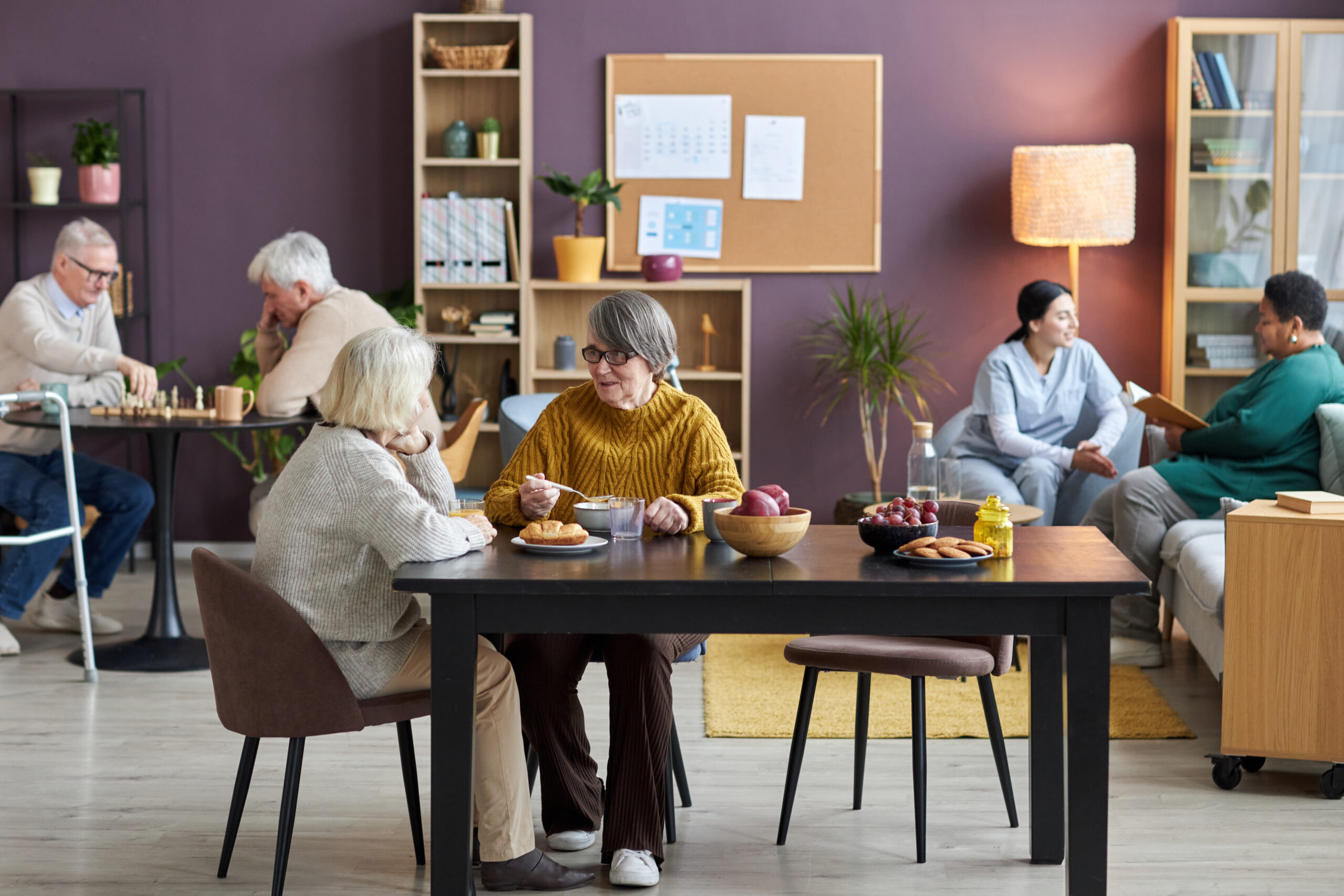Full length view at common room in retirement home with diverse group of seniors enjoying leisure activities