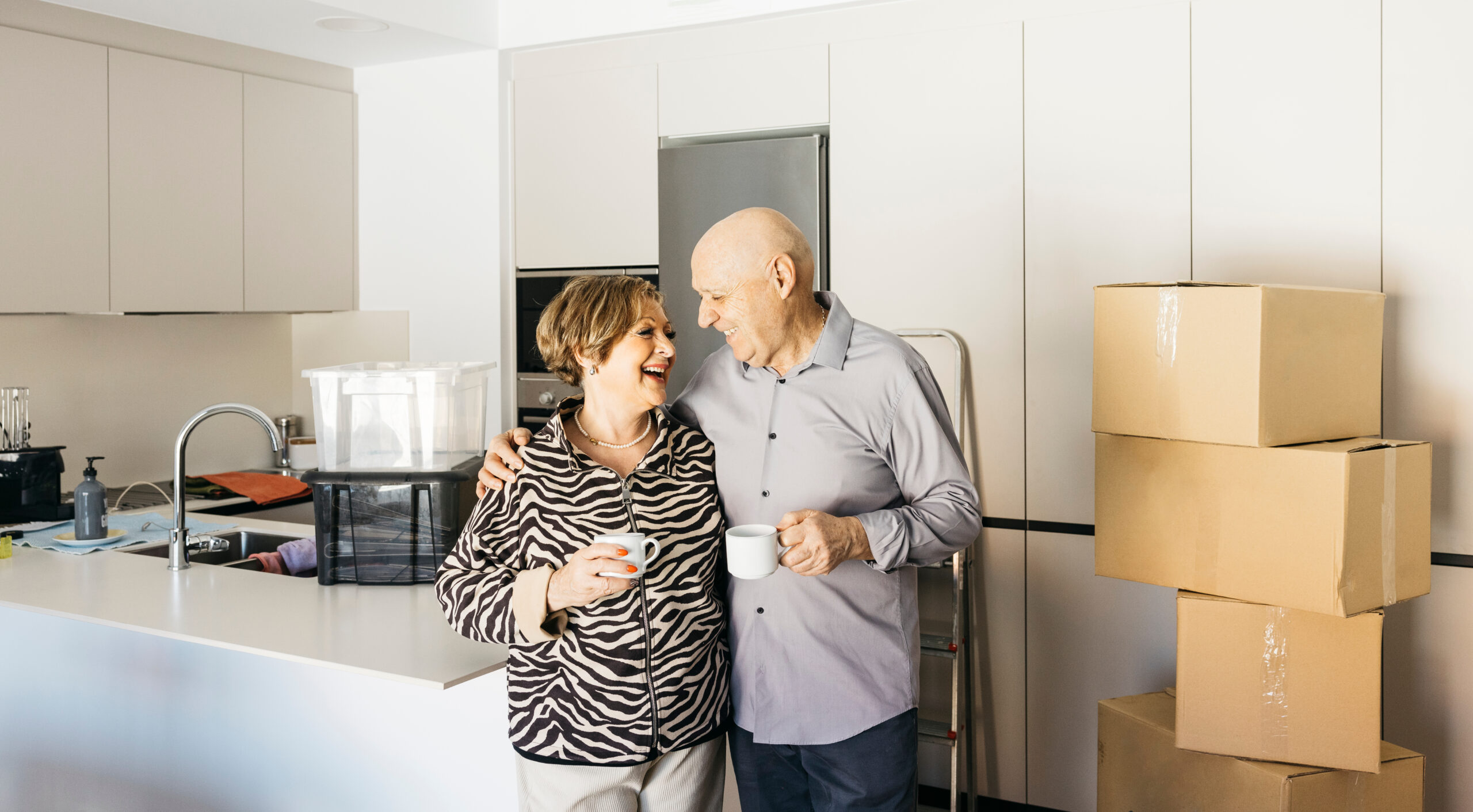 Senior couple embracing and drinking coffee, celebrating moving into new home