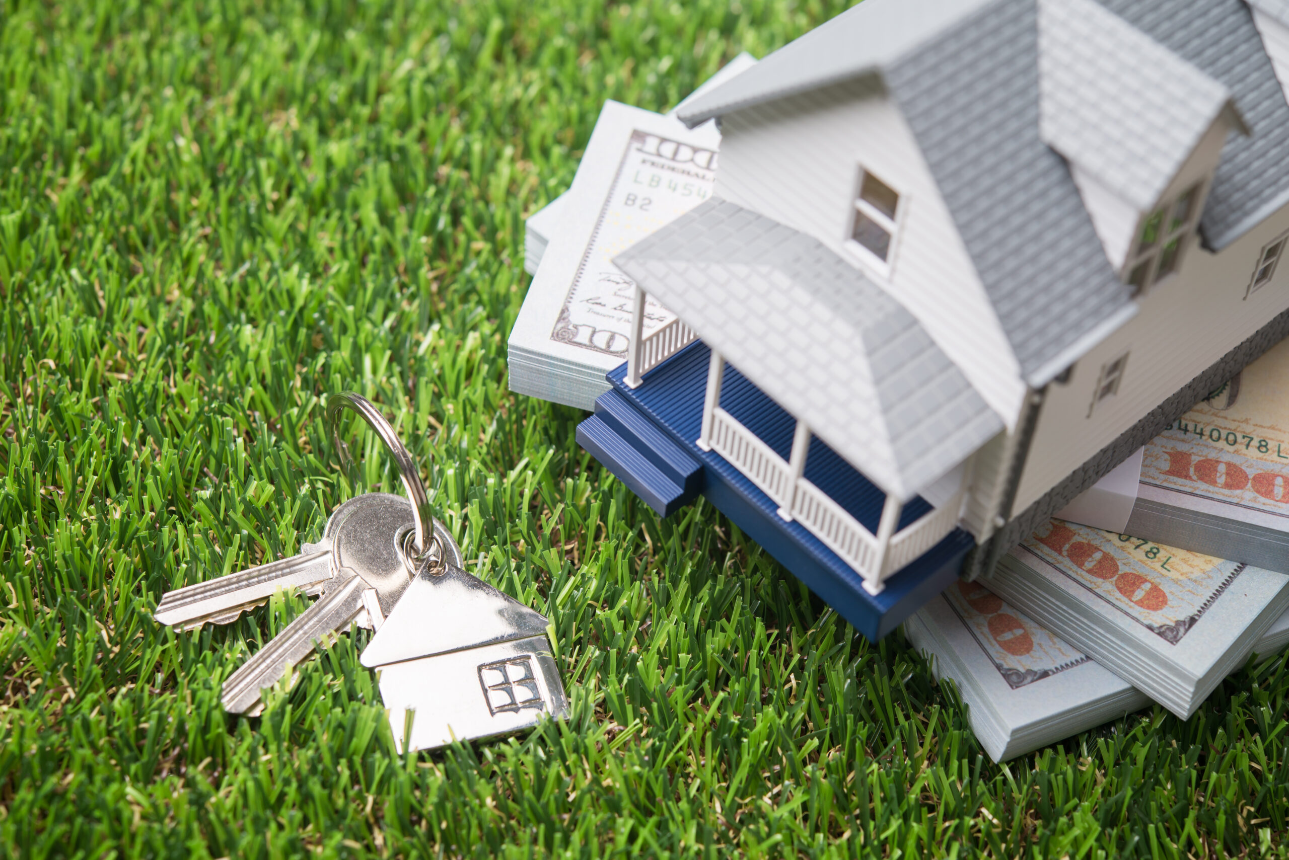 House model, house key and US banknotes on green grass background copy space. Homebuyers, mortgage loan, banking, real estate investment trust (REIT), reverse mortgage, home selling or rental concept.