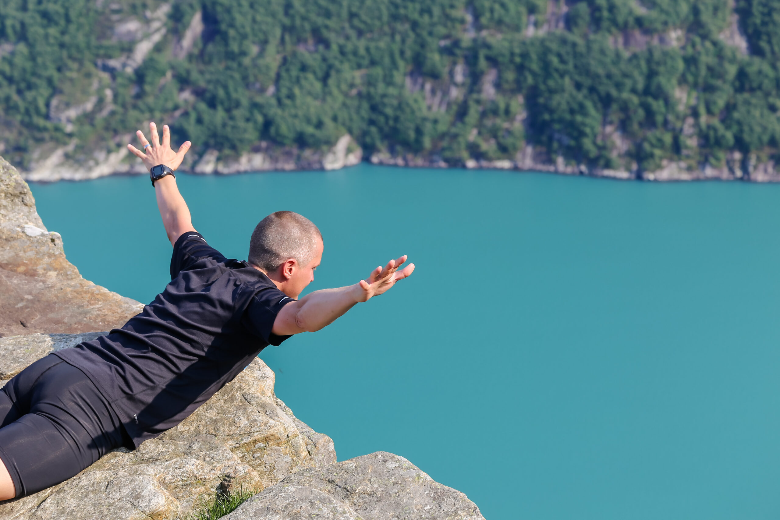 Yung man with arms oustretched at the top of Pulpit Rock peering over the edge of the cliff