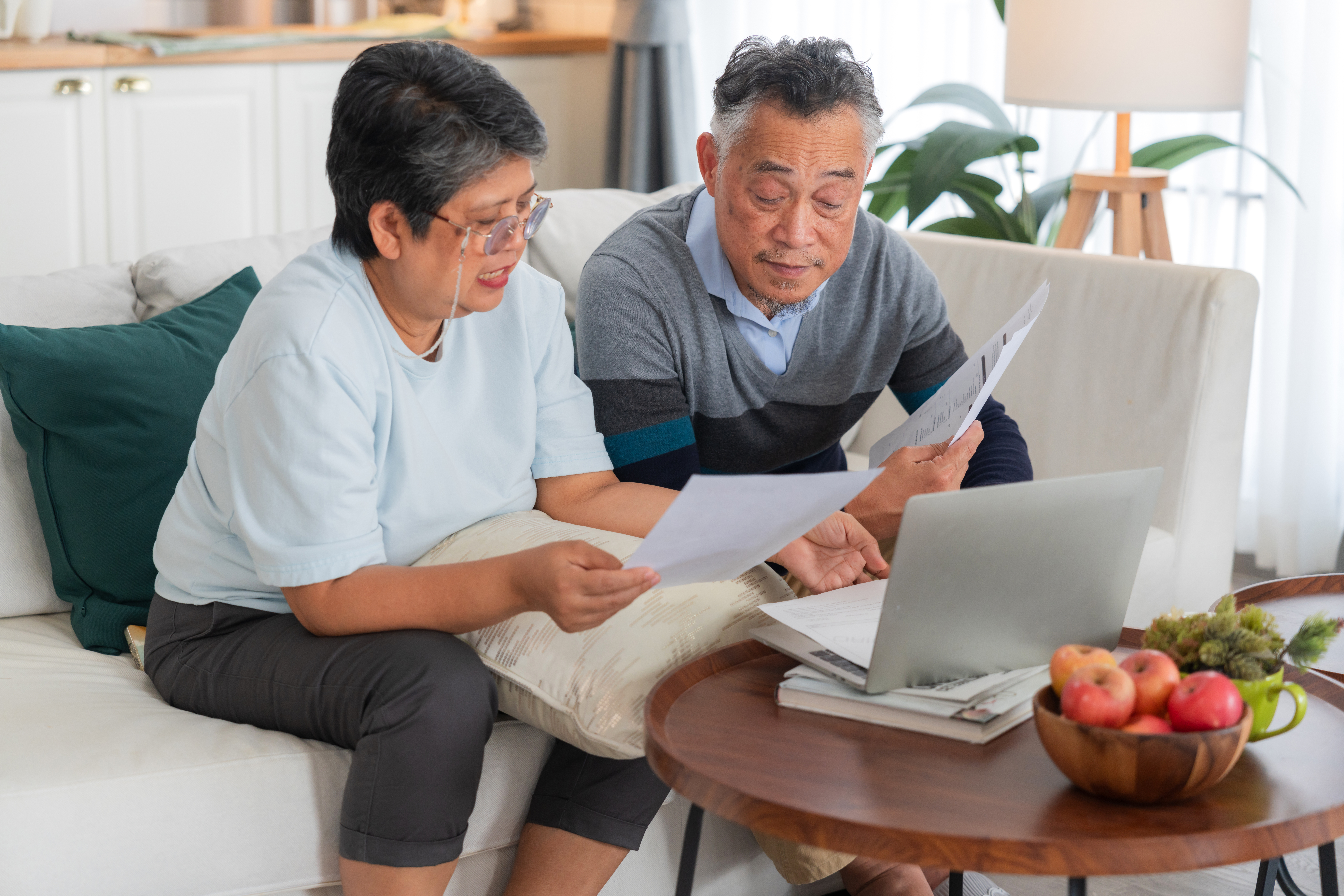 Senior Asian couple reviewing financial documents and bills with laptop computer at home concept for retirement planning savings account budget debt tax form insurance expenses